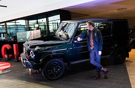 Ein junger Mann lehnt entspannt an einem schwarzen Mercedes-Geländewagen und schaut zur Seite. Der Wagen ist im Ausstellungsbereich mit Scheinwerfern beleuchtet. (Foto: Buchardt | Autohaus Peter )