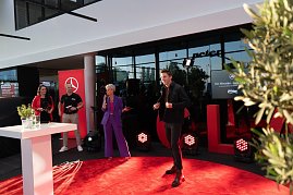 Ein Laufsteg-Moment: Ein junger Mann läuft über den roten Teppich, während Moderatorin Mandy Kossira im lila Hosenanzug mit Mikrofon spricht. (Foto: Buchardt | Autohaus Peter )