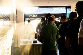 Eine Gruppe Männer steht in einer Schlange am Buffet. Sonnenlicht fällt durch die Tür, im Hintergrund ein Pavillon mit Autohaus-Peter-Logo. (Foto: Buchardt | Autohaus Peter )