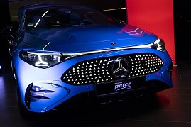 Nahaufnahme der Front eines blauen Mercedes CLA mit beleuchtetem Kühlergrill im Showroom. Ein rotes Eventbanner mit Mercedes-Logo ist im Hintergrund zu sehen. (Foto: Buchardt | Autohaus Peter )