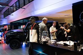Ein Stand mit Mercedes-AMG-Merchandise: Vorne eine Schaufensterpuppe im Trainingsanzug, daneben Besucher, die Kleidung ansehen. Im Hintergrund ein schwarzer Mercedes-Geländewagen. (Foto: Buchardt | Autohaus Peter )