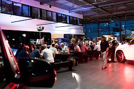 Abendstimmung im Showroom: Viele Gäste sitzen an langen Tafeln, während im Hintergrund Fahrzeuge und Mercedes-Displays beleuchtet sind. (Foto: Buchardt | Autohaus Peter )