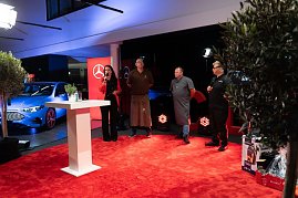 Christina Dost roten Blazer moderiert auf der Bühne. Neben ihr stehen drei Köche und Grillmeister in Schürzen und Arbeitskleidung. Im Hintergrund ein blauer Mercedes. (Foto: Buchardt | Autohaus Peter )