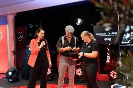 Christina Dost steht mit einem Mann in Schiebermütze und einer Frau im schwarzen Polohemd auf der Bühne. Gemeinsam ziehen sie Lose aus einer Schale. (Foto: Buchardt | Autohaus Peter )