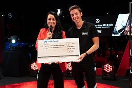 Christina Dost im roten Blazer und ein junger Mann im schwarzen Autohaus-Peter-Shirt präsentieren einen übergroßen Spendenscheck der Volksbank über 1.450 Euro. (Foto: Buchardt | Autohaus Peter )