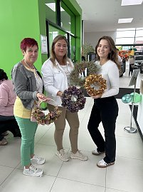 Drei Frauen stehen im Autohaus Autowelt Peter und halten selbstgemachte herbstliche Kränze in den Händen. Im Hintergrund sind weitere Gäste und grüne Luftballons zur Feier von 130 Jahren koda zu sehen. (Foto: Autohaus Peter)