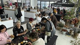 Besucherinnen und Besucher gestalten herbstliche Gestecke und Kränze an Basteltischen im Autohaus Autowelt Peter. Auf den Tischen liegen Kürbisse, Zweige und Blumen. Im Hintergrund sind weitere Stände und ein Fahrradbereich mit SCOTT-Zelt zu sehen. (Foto: Autohaus Peter)