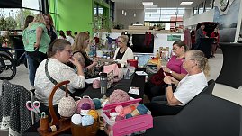 Frauen sitzen an einem Tisch im Autohaus Autowelt Peter und stricken gemeinsam. Auf dem Tisch liegen bunte Wollknäuel, Strickutensilien und Handarbeiten. Im Hintergrund sind weitere Gäste und Ausstellungsstände zu sehen. (Foto: Autohaus Peter)