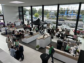 Blick von oben in den hellen Ausstellungsraum des Autohauses Autowelt Peter während der Feier zu 130 Jahren koda. Besucherinnen und Besucher sitzen an Tischen, basteln und stricken, andere informieren sich an Ständen, darunter ein SCOTT-Zelt mit Fahrrädern. (Foto: Autohaus Peter)