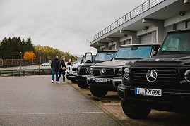 Noch einmal eine professionelle Aufnahme aller G-Klassen Modelle aufgereiht im sauberen Zustand vor der G-Klassen experience. Einige Teilnehmer schauen sich zudem die Modelle an. [Mercedes-Benz G 580 mit EQ Technologie | Energieverbrauch kombiniert: 30,3-27,7 kWh/100 km | CO2;-Emissionen kombiniert: 0 g/km | CO2;-Klasse: A] [Mercedes-AMG G 63 | Energieverbrauch kombiniert: 15,7-14,7 l/100 km | CO2;-Emissionen kombiniert: 358-335 g/km | CO2;-Klasse: G]  (Foto: Mercedes-Benz AG)