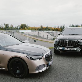 Zwei Luxusautos von Mercedes-Benz stehen nebeneinander auf einer Rennstrecke. Auf der linken Seite ist ein silberner Mercedes-Maybach S-Class zu sehen, der eine glänzende schwarze Motorhaube und schwarze Räder hat. Rechts daneben steht ein schwarzer Mercedes-Maybach GLS, ein großer SUV mit auffälligem Kühlergrill und silbernen Akzenten. Im Hintergrund erstreckt sich die Rennstrecke, und Bäume mit herbstlichen Farben sind am Horizont sichtbar. (Foto: © 2025 HANSE VISUALS)