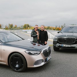 Zwei Männer stehen lächelnd nebeneinander zwischen zwei Mercedes-Maybach Fahrzeugen auf dem Gelände der Mercedes-Benz Driving Experience am Bilster Berg. Im Hintergrund ist die Rennstrecke mit herbstlicher Landschaft zu sehen. (Foto: © 2025 HANSE VISUALS)