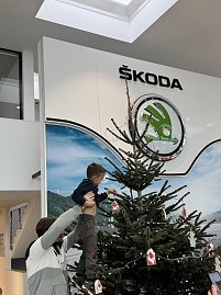 Ein Erzieher hebt das Kind hoch, damit es weiter oben am Baum seinen Anh&auml;nger platzieren kann.