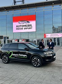 Schwarzer Opel-SUV vor der Messe Erfurt, im Hintergrund LED-Schild Automobil Messe Erfurt, zwei M&auml;nner im Gespr&auml;ch.