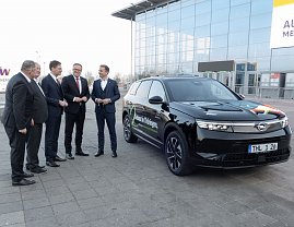F&uuml;nf M&auml;nner im Anzug stehen vor der Messehalle neben einem schwarzen Opel-SUV mit der Aufschrift Gebaut in Th&uuml;ringen.