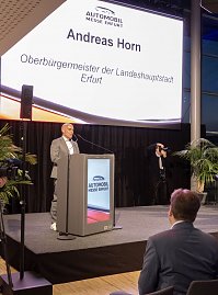 Mann am Rednerpult auf der B&uuml;hne der Automobil Messe Erfurt, Leinwand zeigt Andreas Horn, Oberb&uuml;rgermeister Erfurt.