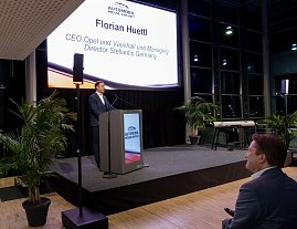 Mann am Rednerpult auf der B&uuml;hne der Automobil Messe Erfurt, Leinwand: Florian Huettl, CEO Opel und Director Stellantis 