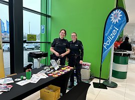 Zwei Polizistinnen stehen an einem Infostand mit Buttons und Malmaterial, daneben Banner Th&uuml;ringer Polizei.