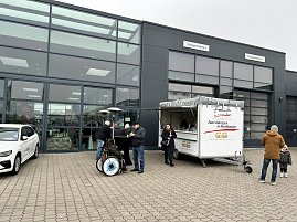 Mehrere Besucher neben einem Foodtruck und Stehtischen auf dem Autohaus-Parkplatz.