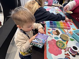 Kleines Kind bastelt am Tisch mit Perlen, daneben liegen Schalen und Bastelmaterial.