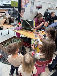 Mehrere Kinder stehen an einem Aktionsstand, w&auml;hrend eine Frau einem Jungen das Gesicht schminkt. Auf dem Tisch liegen Farben, Flyer und Zubeh&ouml;r. 