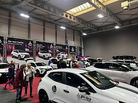 Mehrere wei&szlig;e Mitsubishi-Fahrzeuge in einer Messehalle, dazwischen interessierte Messebesucher, vorn ein schwarzes Autocenter Peter Logo.