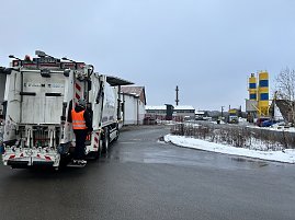 Verkaufsberater vom Autohaus Peter Andr&eacute; Schmidt steht auf der Trittstufe eines M&uuml;llfahrzeugs w&auml;hrend der Fahrt durch ein Industriegebiet.