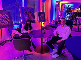 Zwei Personen an Tisch in Lounge mit bunter Eventbeleuchtung und Kunstwerken.