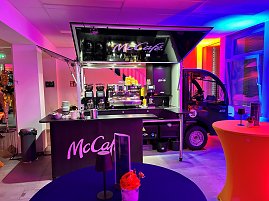 cCafé-Kaffeebar im Eventbereich mit buntem Licht und Stehtischen.