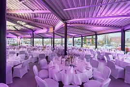 Großer Eventsaal mit gedeckten runden Tischen und lila Beleuchtung.