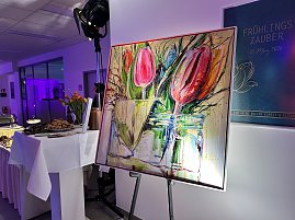 Gemälde mit Tulpen auf Staffelei neben Buffet im Eventbereich.