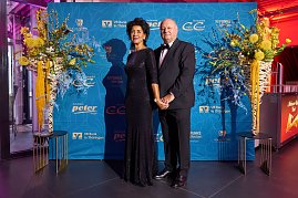 Elegant gekleidetes Paar vor Sponsorenwand bei Event mit Blumendekoration.