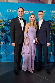 Drei elegant gekleidete Personen vor Sponsorenwand bei Event.