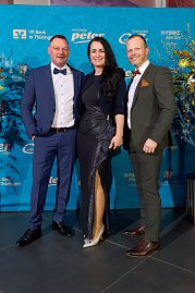 Drei elegant gekleidete Personen vor Sponsorenwand bei Event.