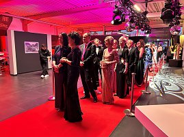 Elegant gekleidete Gäste auf rotem Teppich im Eventbereich mit Beleuchtung.