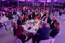Gäste sitzen an gedeckten Tischen bei Gala-Event mit stimmungsvoller Beleuchtung.