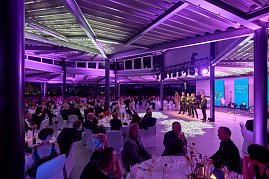 Gala-Event mit Bühne, Rednern und Publikum an gedeckten Tischen.