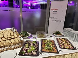 Buffet mit Salaten, Brot und Vorspeisen neben Willkommensschild.