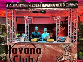 Ein stilvoller Cocktail-Stand im Havana-Club-Design: Zwei Barkeeper stehen hinter der Bar und servieren vorbereitete Drinks.