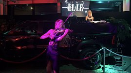 Close-up der Performance: Eine Violinistin spielt energiegeladen vor einem inszenierten Pickup, während im Hintergrund eine DJane auflegt.