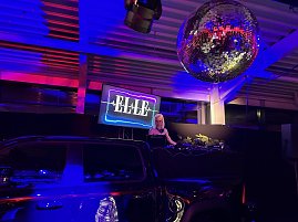 Stimmungsvolle Club-Inszenierung: Eine DJane performt hinter dem Pult, während eine große Discokugel das Licht in den Raum reflektiert.