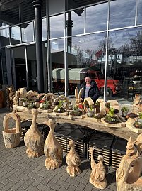 Ein Stand mit verschiedenen Skulpturen aus Holz, dahinter steht eine Frau und l&auml;chelt in die Kamera.