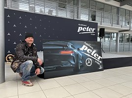 Alex Sitt hockt neben dem fertigen Graffiti-Bild. Auf dem Bild ist ein Pkw von hinten zu sehen, daneben ist das Logo der Autohaus Peter Gruppe.