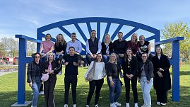 Gruppenfoto: Gro&szlig;e blaue XXL-Bank, darauf sitzen mehrere Personen, einige stehen davor und l&auml;cheln in die Kamera.