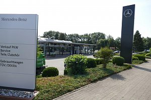 Au&szlig;enansicht des Mercedes-Benz Autohauses Duderstadt mit gro&szlig;em Mercedes-Stern auf einer hohen Stele und einem Wegweiser, der auf Verkauf PKW, Service, Teile/Zubeh&ouml;r, Gebrauchtwagen sowie T&Uuml;V/DEKRA hinweist. Im Hintergrund ein modernes, verglastes Autohausgeb&auml;ude, umgeben von gepflegten Gr&uuml;nfl&auml;chen und B&uuml;schen.