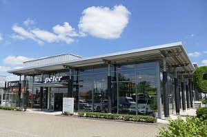 Modernes Mercedes-Benz Autohaus mit gro&szlig;er Glasfassade und der Aufschrift �peter� &uuml;ber dem Eingang. Links daneben ein Bereich mit Smart-Logo. Vor dem Geb&auml;ude gepflegte Gr&uuml;nfl&auml;chen, blauer Himmel mit wenigen wei&szlig;en Wolken.