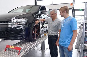 Mitarbeiter in der Werkstatt des Škoda Autohauses erklärt einem Kunden die Profiltiefe eines Reifens an einem schwarzen Auto auf der Hebebühne.