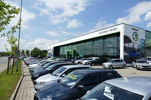 Großes Škoda-Autohaus ‚Autowelt Peter‘ mit moderner Glasfassade und grünem Eingang. Davor stehen viele Neuwagen und Gebrauchtwagen in mehreren Reihen auf dem Parkplatz.