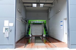 Moderne Waschanlage mit grünem Schriftzug ‚Autopflege‘ in einer hellen Halle, bereit für die Fahrzeugreinigung.