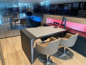 Modern eingerichtetes Verk&auml;uferb&uuml;ro im Autohaus mit hellem Holzboden, stilvollem Tisch, bequemen St&uuml;hlen und Computerarbeitsplatz. Im Hintergrund Glaswand mit Punktmuster.